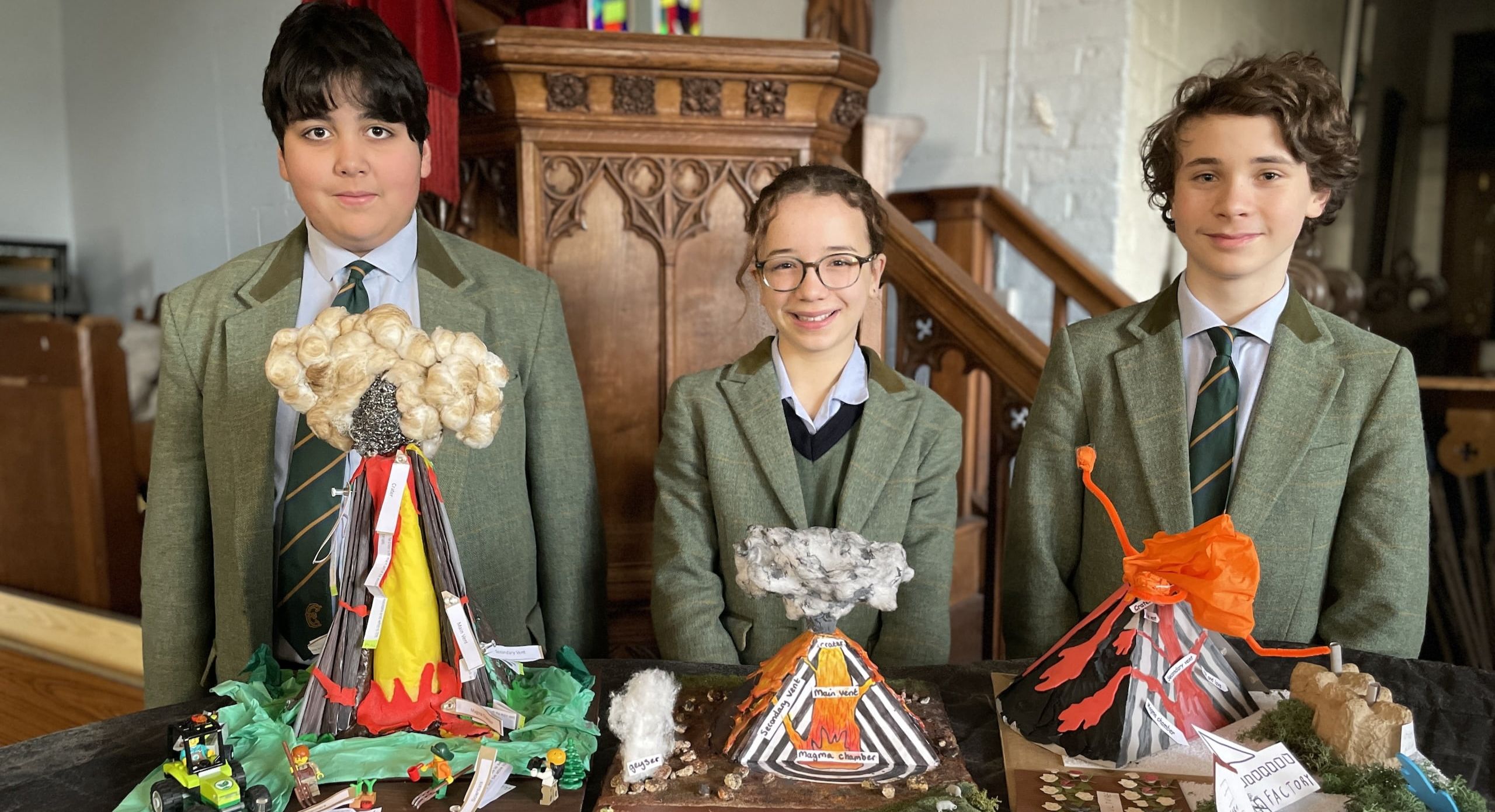 Three students stand in front of their Geography project of volcano cross sections